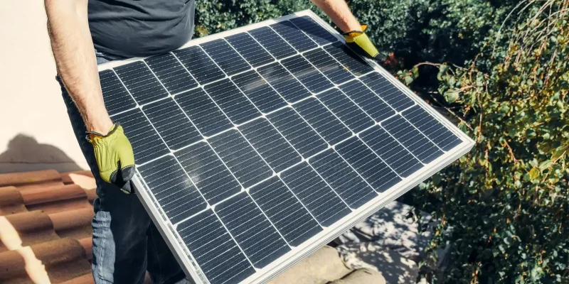 Photo by Kindel Media A worker in gloves installs a solar panel on a tiled rooftop, promoting renewable energy.